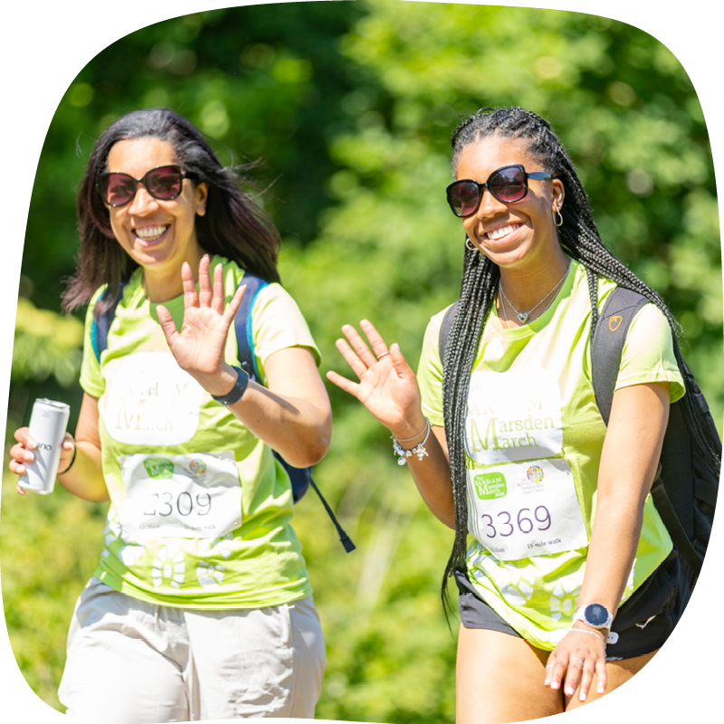 Two Banham Marsden Marchers, walking through a park. They are smiling and waving