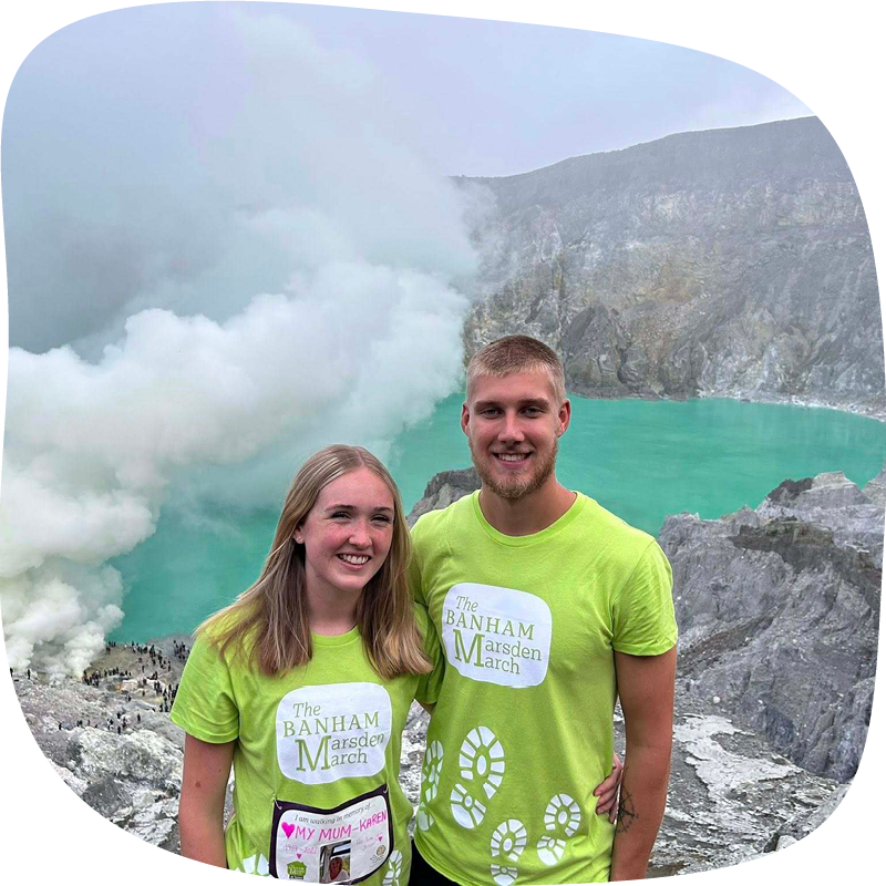 Two people taking part in the Banham Marsden March at home. They are standing in front of a beautiful view of a volcanic lake