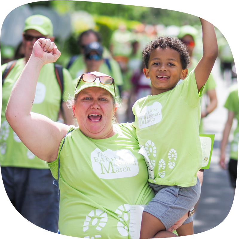Banham Marsden Marcher holding a small child, they're both smiling and throwing their fists up in the air.
