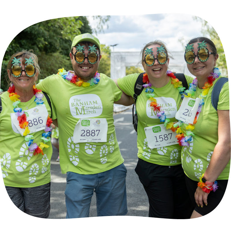 Four Banham Marsden Marchers with their arms around each other. They're wearing palm tree glasses and flower necklaces