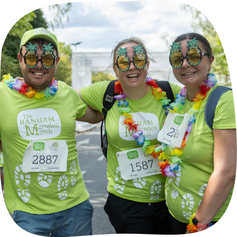 Three Banham Marsden Marchers with their arms around each other. They're wearing palm tree glasses and flower necklaces